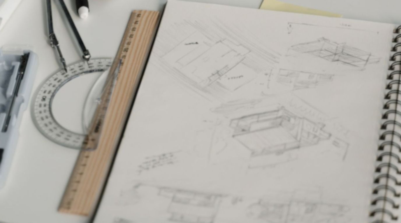 Pencil sketches in a notebook beside a ruler, compass and protractor